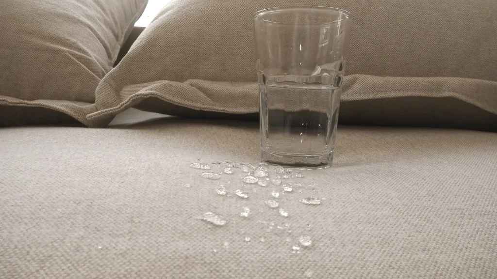 Sofá impermeabilizado com gotas d'água sob o tecido impermeável e um copo ao lado.